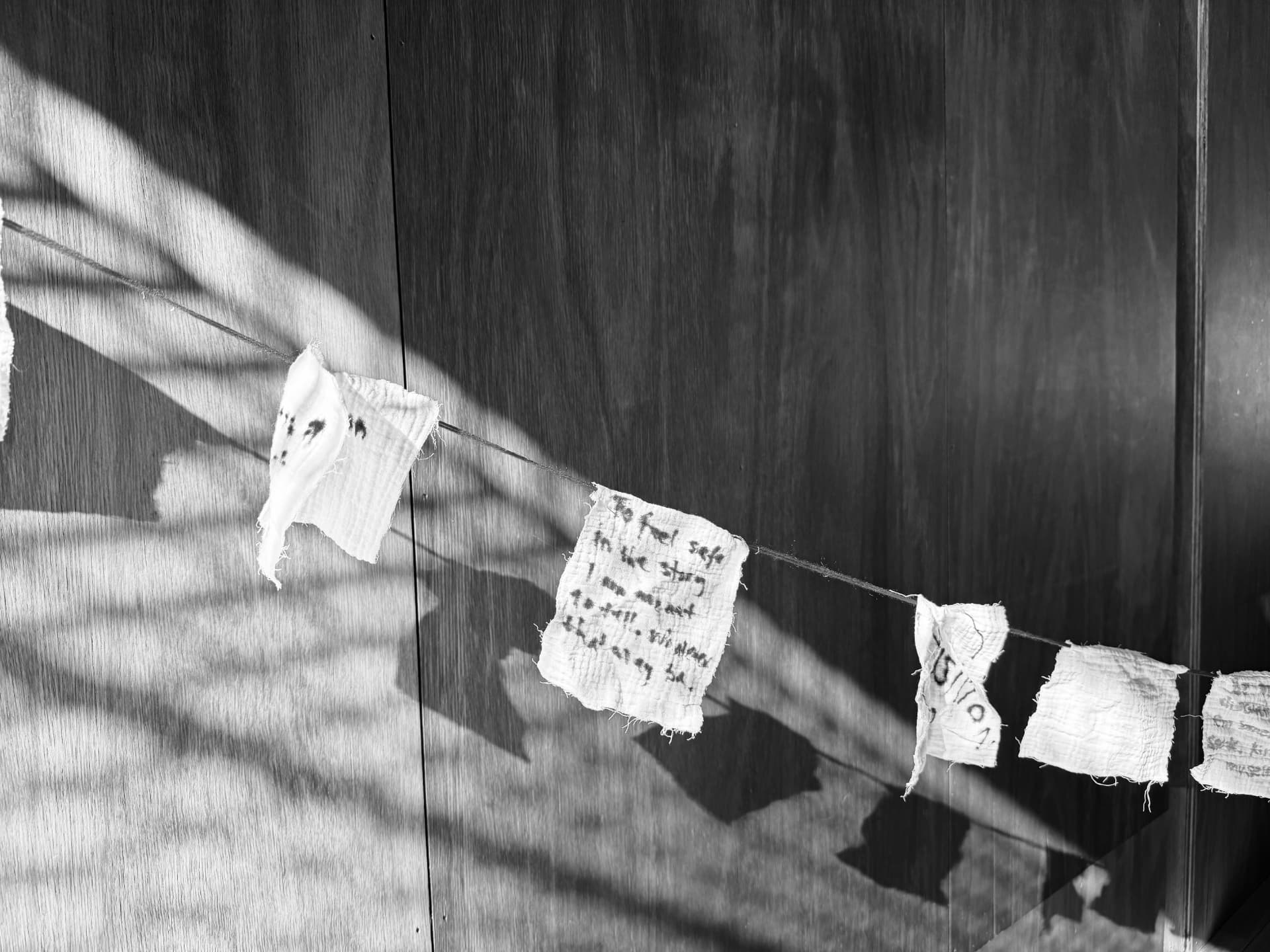 Handwritten notes on small fabric prayer flags strung across a wooden wall