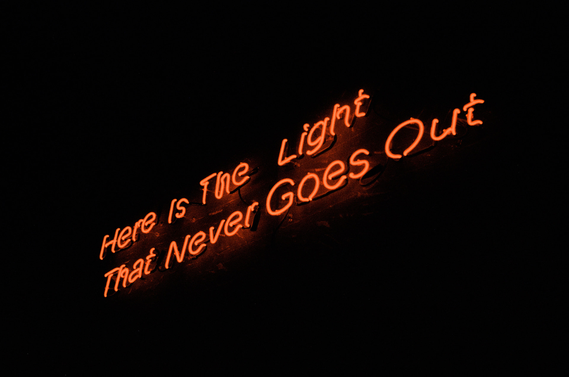 Neon sign glowing in the dark reading 'Here is the light that never goes out'